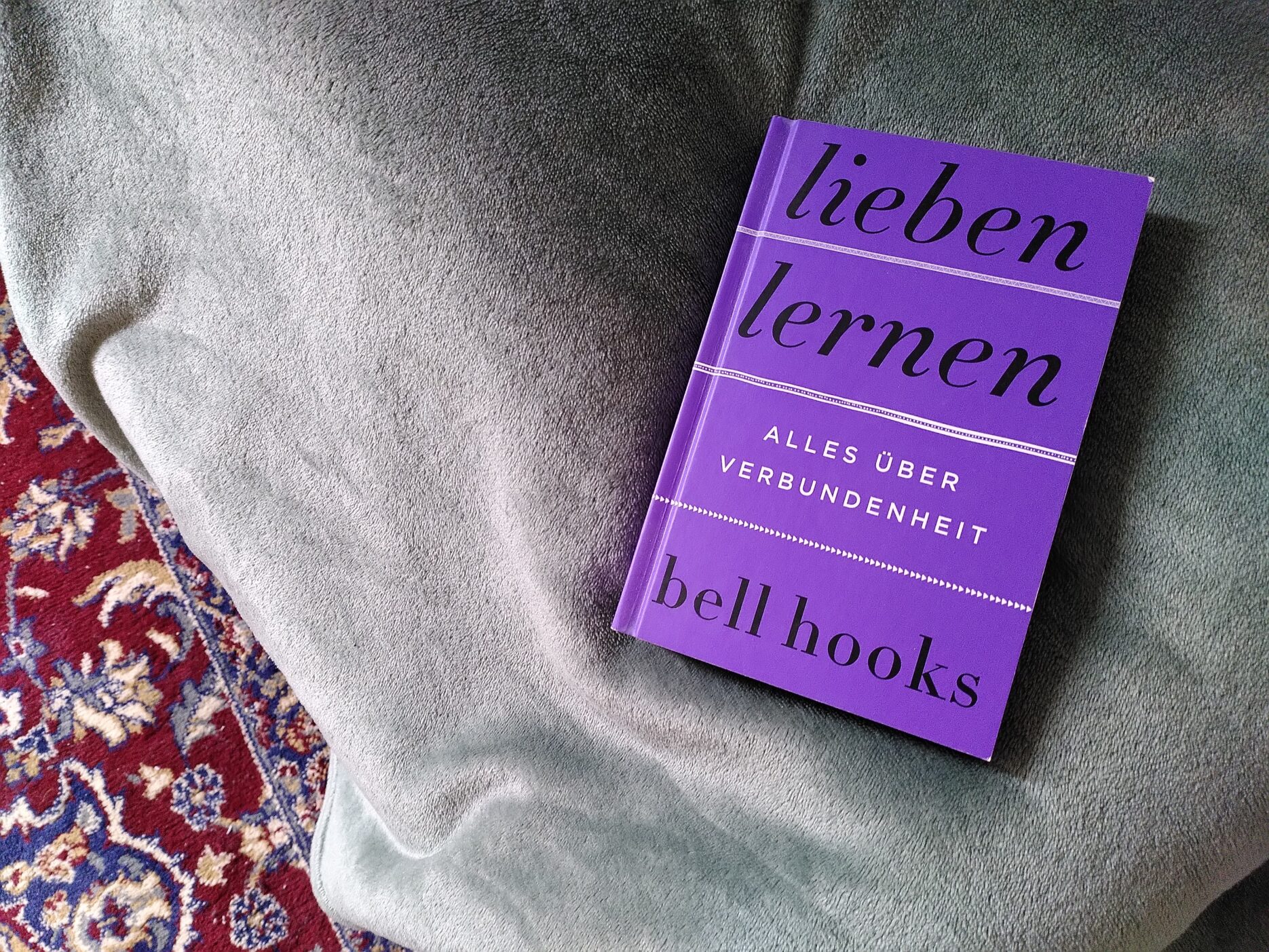 Das Buch "Lieben lernen" von bell hooks liegt auf einem Bett.