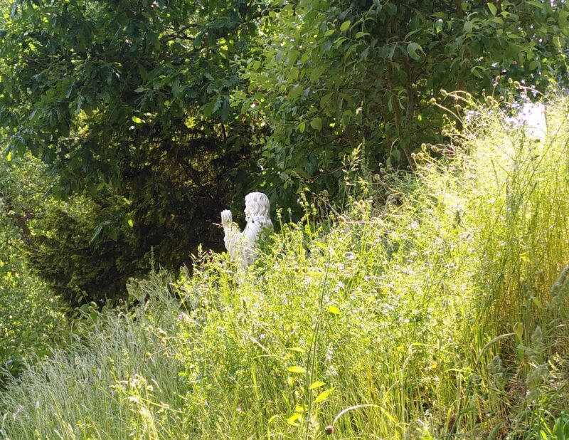 Eine Jesus-Statue halb versteckt im hohen Gras einer Sommerwiese
